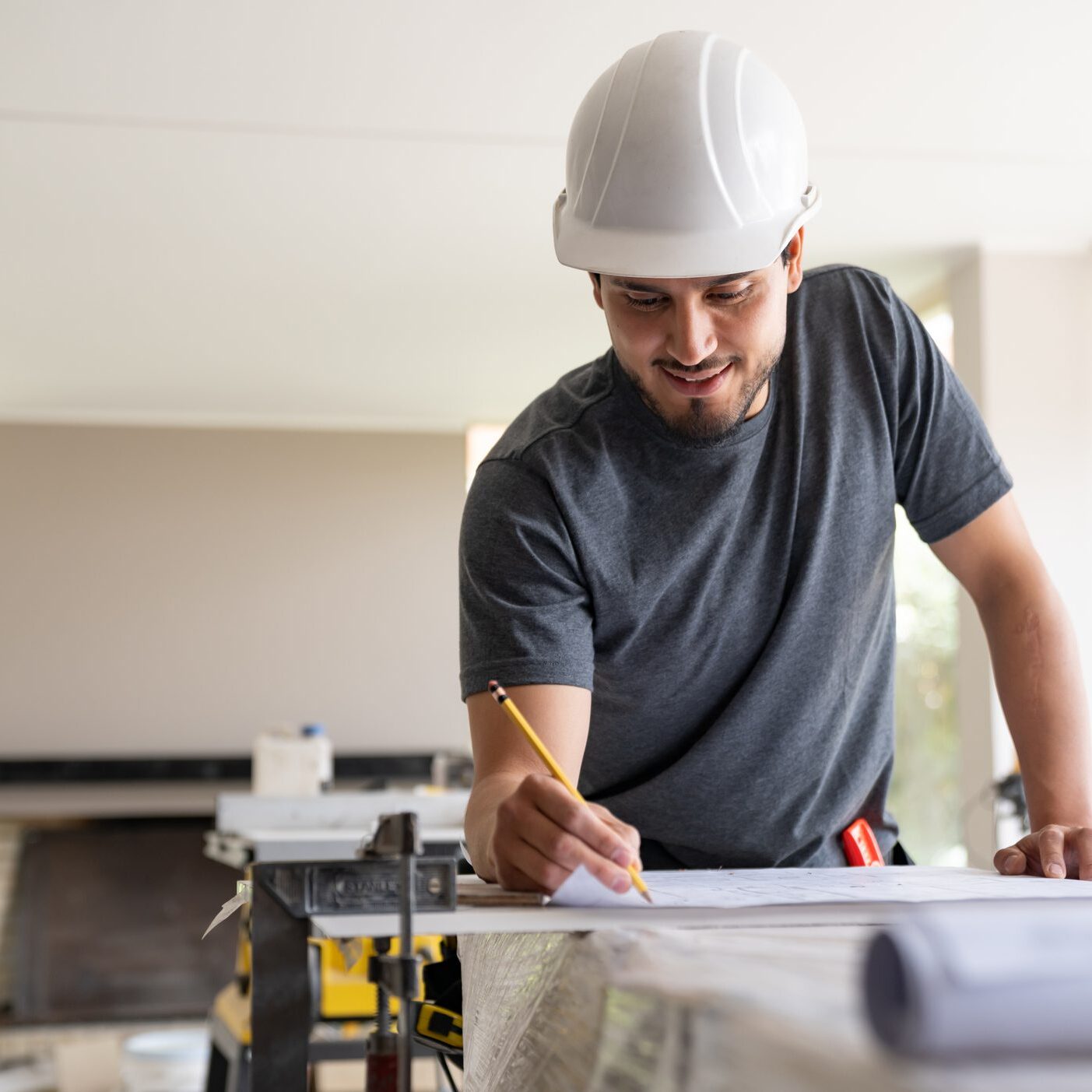 Happy Latin American civil engineer drawing on blueprints while building a house - construction concepts